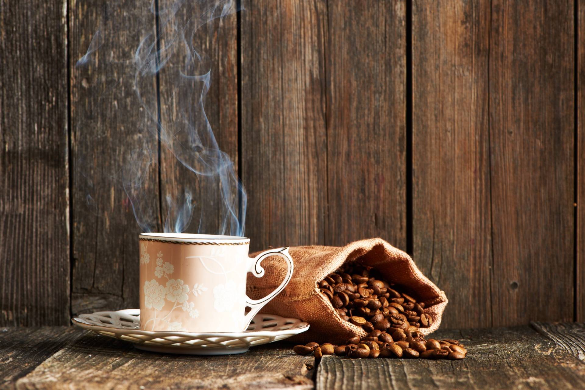 A steaming cup beside a small burlap sack of beans on a weathered wooden table