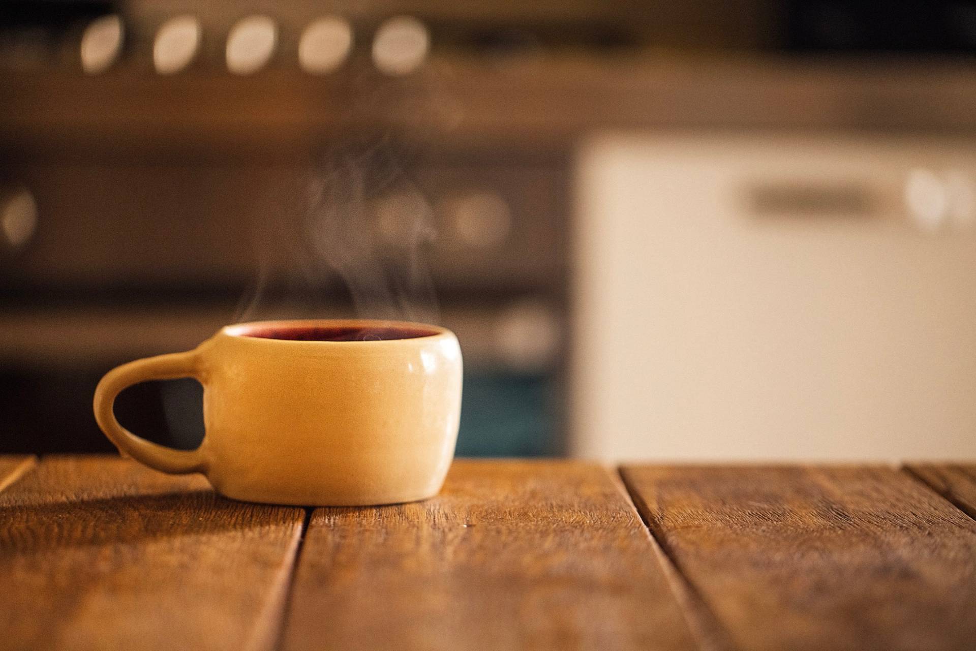 A yellow ceramic mug steaming on a wooden kitchen table